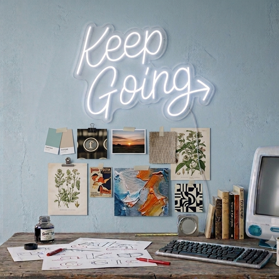 Neon sign reading 'Keep Going' above a desk with various items and wall art.