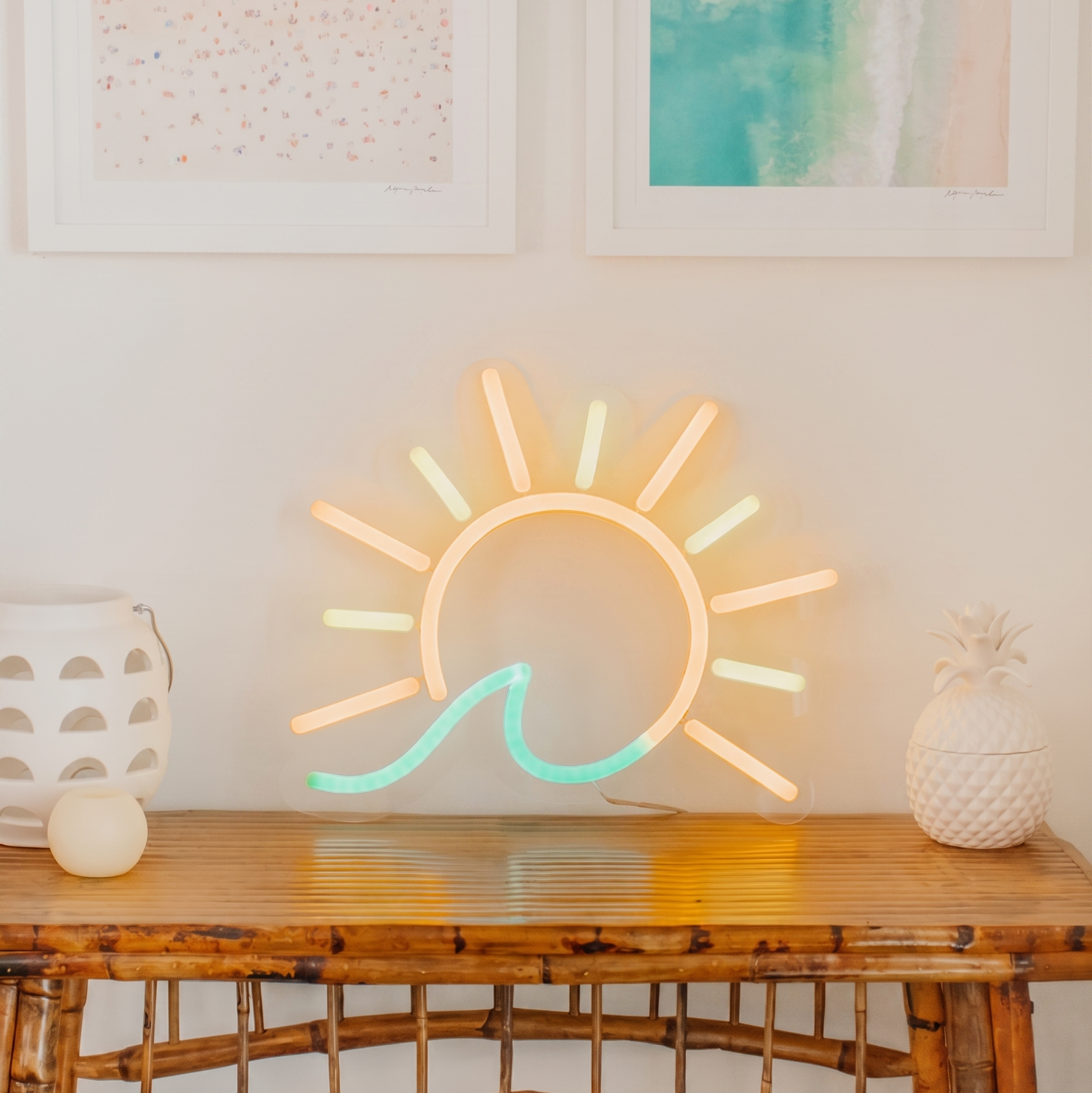Neon sun light fixture on a wooden console table with framed abstract art in the background.