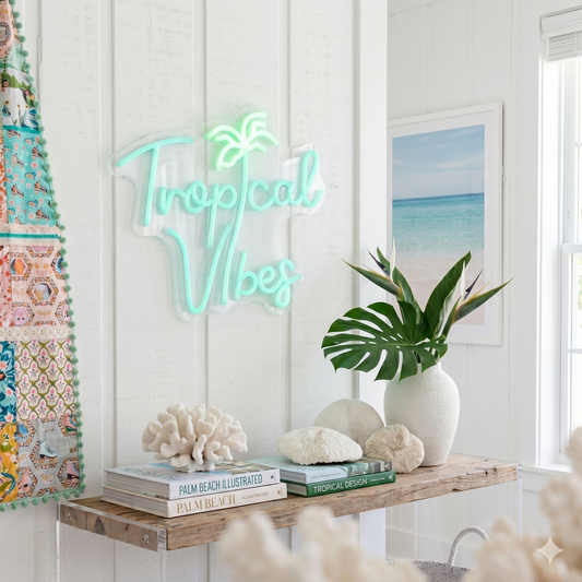 Neon 'Tropical Vibes' sign in a room with decor elements like books, plants, and a beach-themed picture.