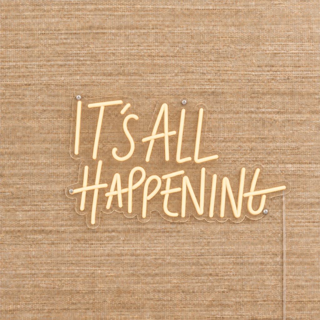 Champagne It’s All Happening LED neon sign on beige woven wallpaper with clear acrylic backing and silver mounting screws.